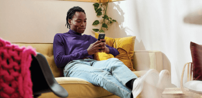 A man sits on his couch in his living room while looking at his phone