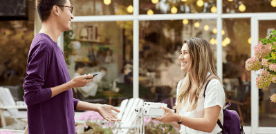 A man and a woman stand in front of an outdoor table talking